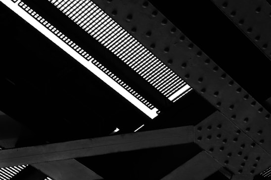 Detailed view of a steel structure with intersecting girders and a grated surface, showing patterns of bolts and rivets.