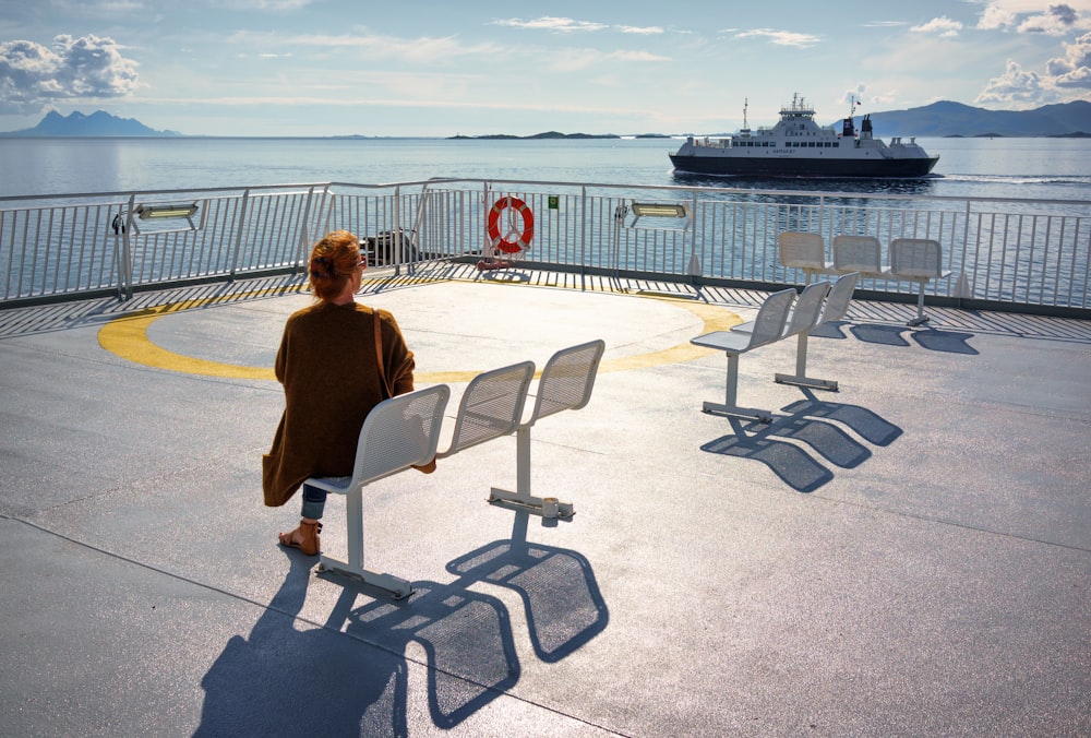 woman in brown cardigan sitting on white steel chair looking at the boat on the sea