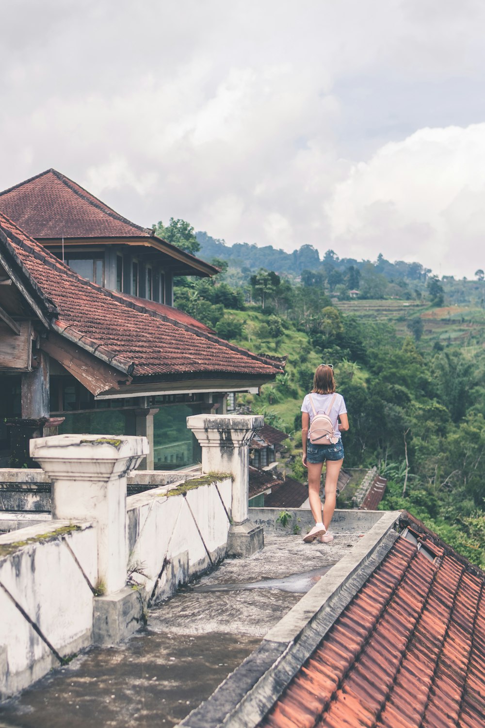 woman standing on edge of building facing land covered with trees