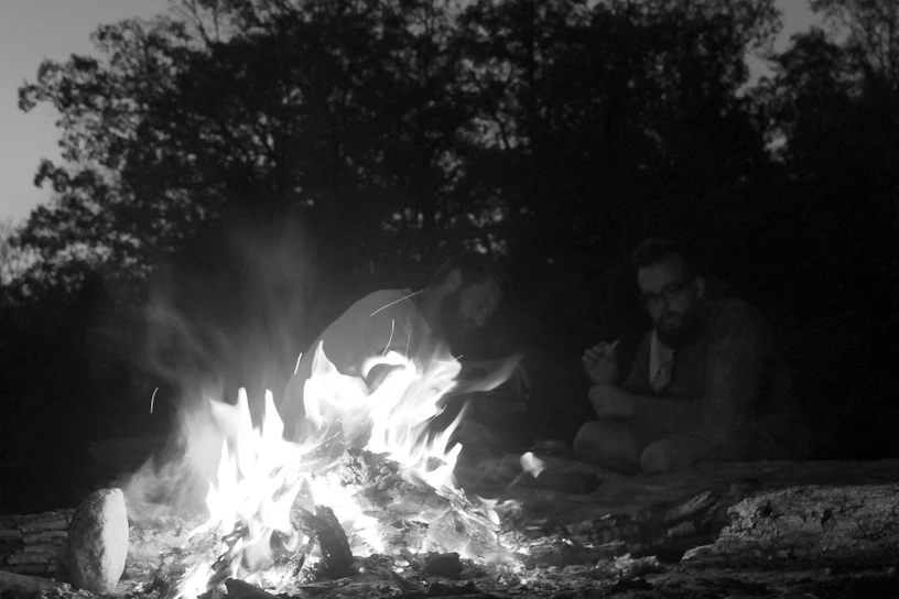 Black and white photo of WWII soldiers from the unit gathered around a campfire, sharing stories.