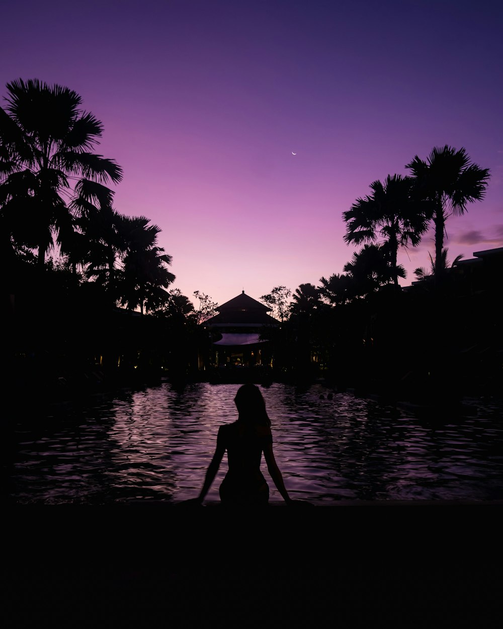 Silhouette einer Frau, die nachts am Rand des Pools sitzt