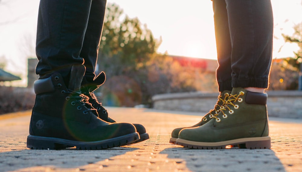 two people wearing green-and-black work boots standing on gray concrete pavement