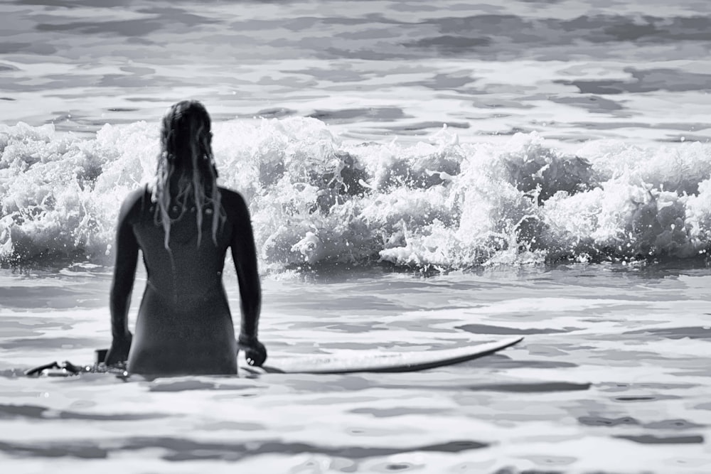 grayscale photography of woman in ocean holding surfboard