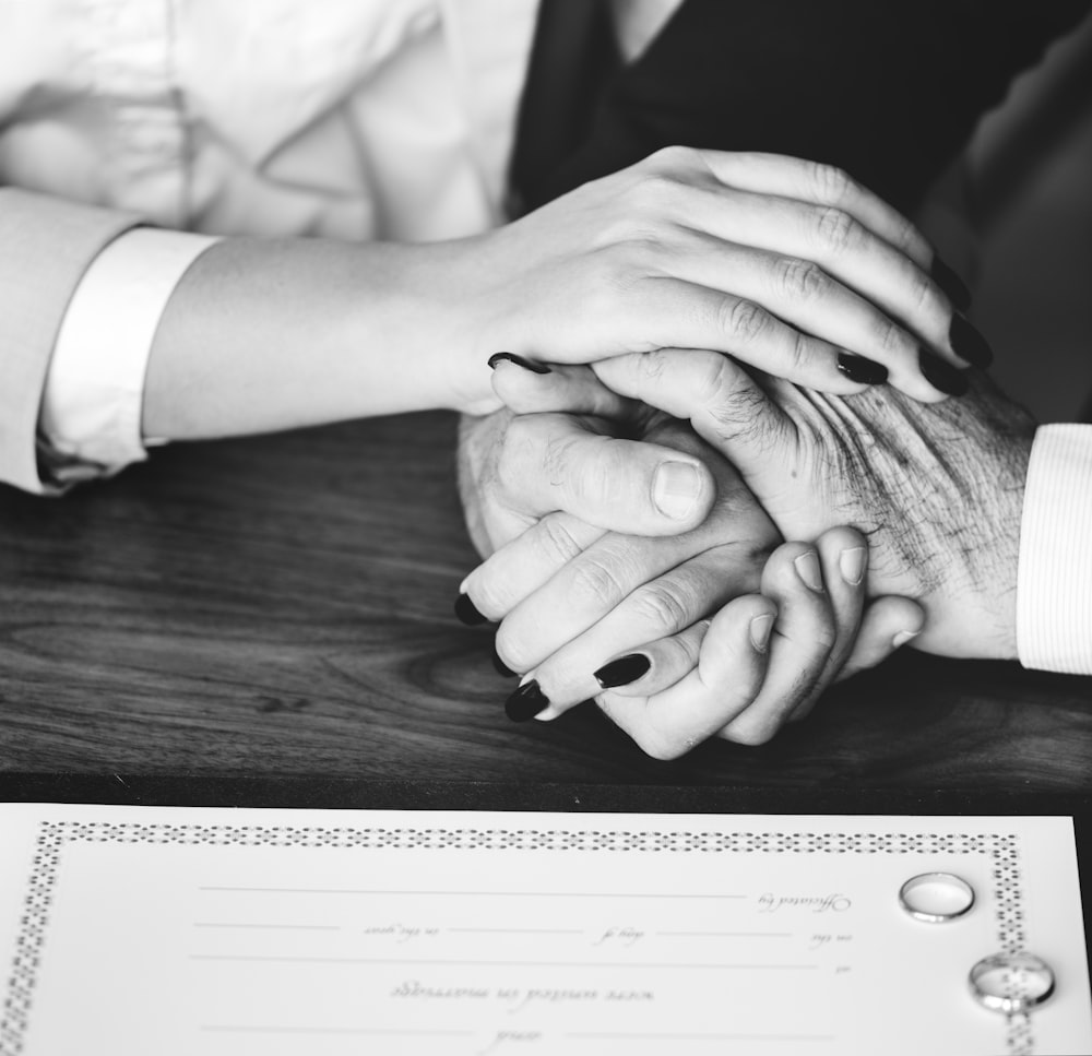 grayscale photo of two person hand holding hands beside two rings