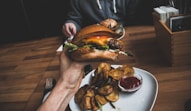 person holding burger filled with sliced tomato and lettuce