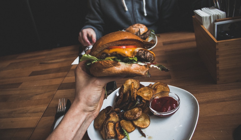 person holding burger filled with sliced tomato and lettuce