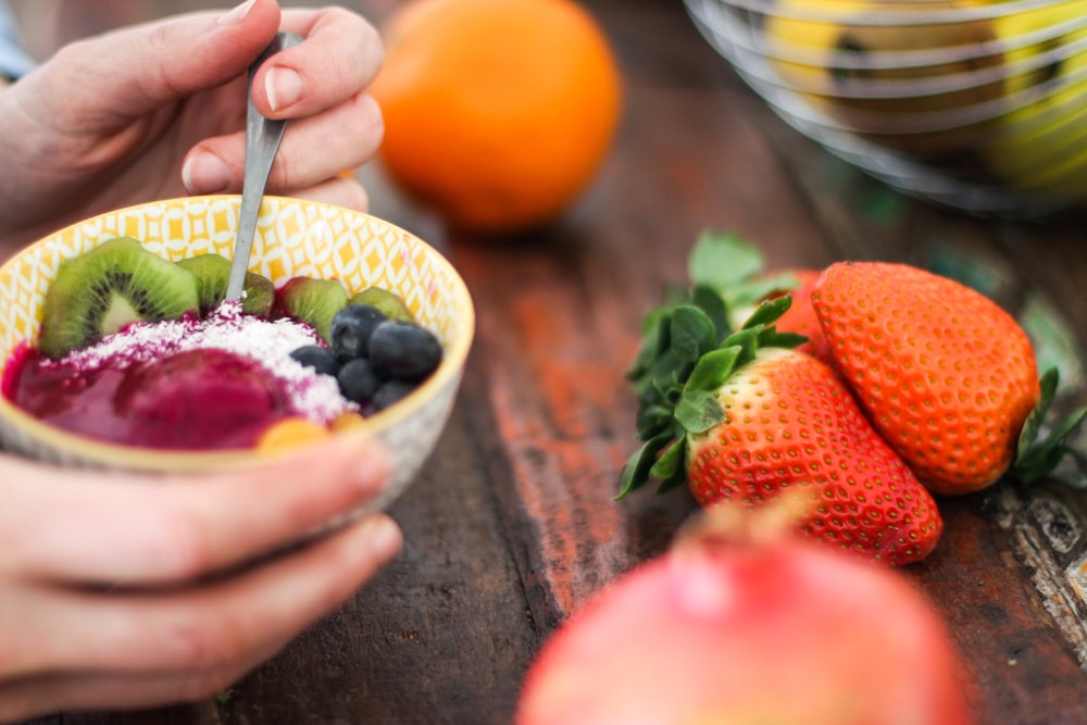 personne tenant une salade de fruits tranchés sur un bol jaune