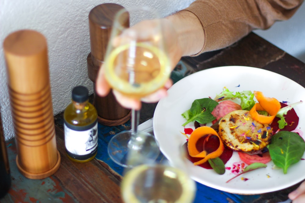 Persona sosteniendo una copa de vino frente a la ensalada de verduras