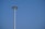 A tall, modern street light extends against a clear blue sky, featuring a circular array of lights at the top.