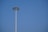 A tall, modern street light extends against a clear blue sky, featuring a circular array of lights at the top.
