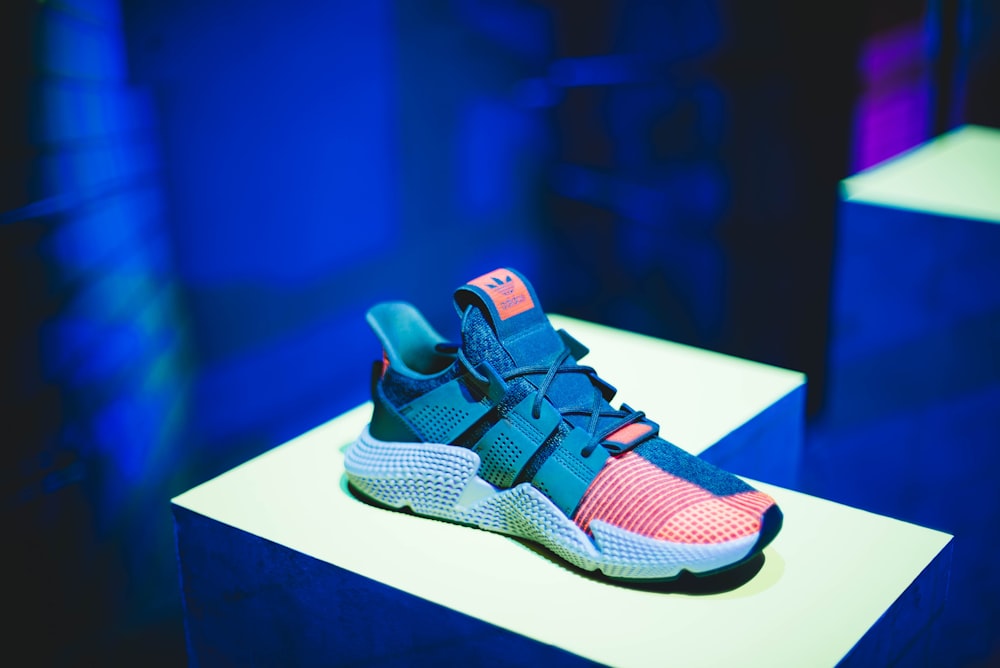 blue, pink, and white adidas athletic shoe on white display table