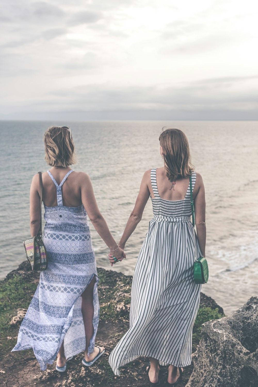 two woman in maxi dresses holding each other hand while standing on cliff