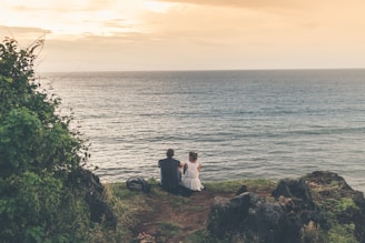 man sitting beside woman both facing in front of body of water