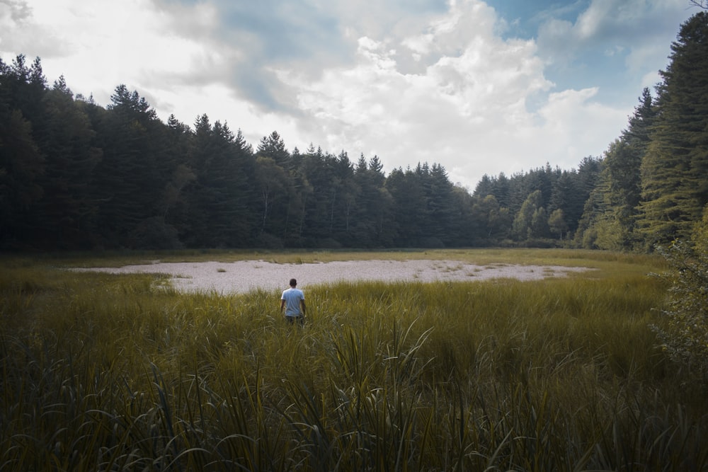 man walking on tall grass near pond during daytime