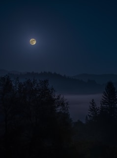 A glowing full moon over a quiet landscape, symbolizing lunar cycles and inner listening.