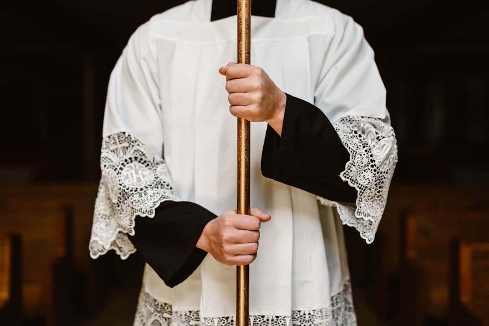 person wearing white surplice holding rod