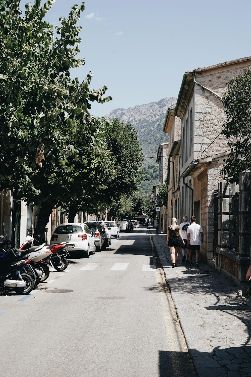 three person walking near road beside brown concrete house at daytime