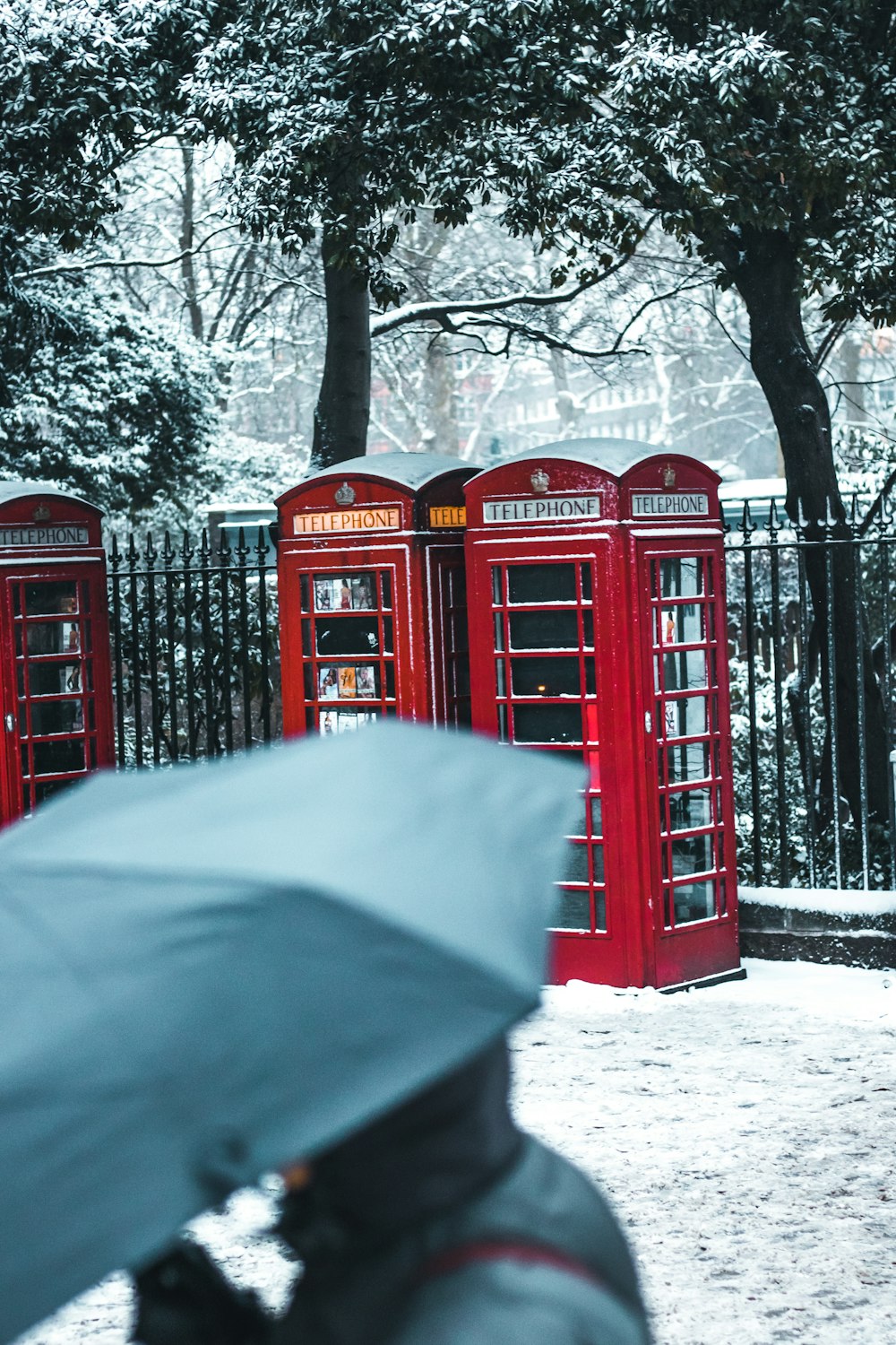 red telephone booths behind black steel fence during snow season