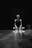 A person is sitting cross-legged on a wooden floor with a focused expression. The setting is dark with a spotlight creating reflections on the polished surface. The scene suggests solitude and introspection.