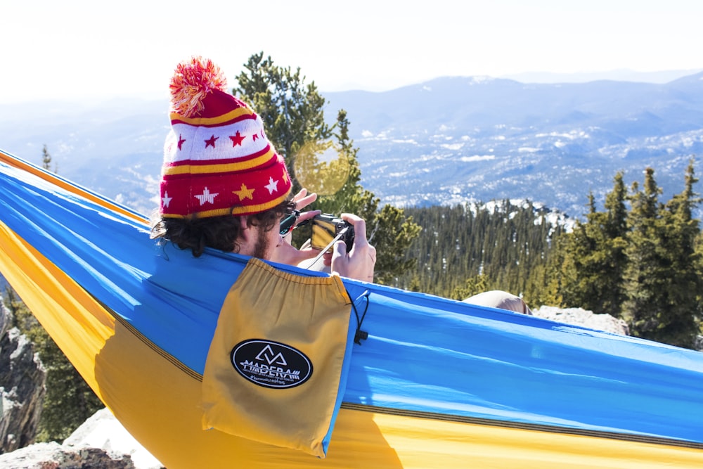 man in red and white bobble knit cap on blue and yellow hammock