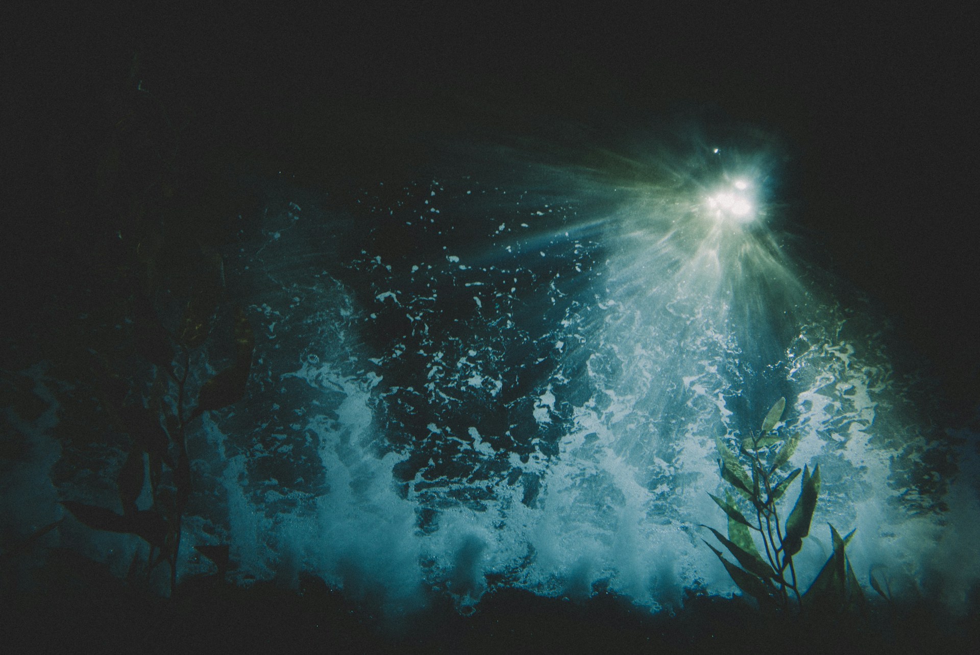 A mysterious underwater scene with a bright light creating dramatic rays through the water, illuminating bubbles and plants. The atmosphere is deep and captivating with aquatic reflections.