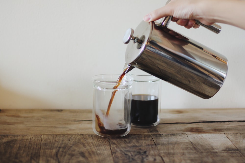 persona que vierte café en una taza de vidrio