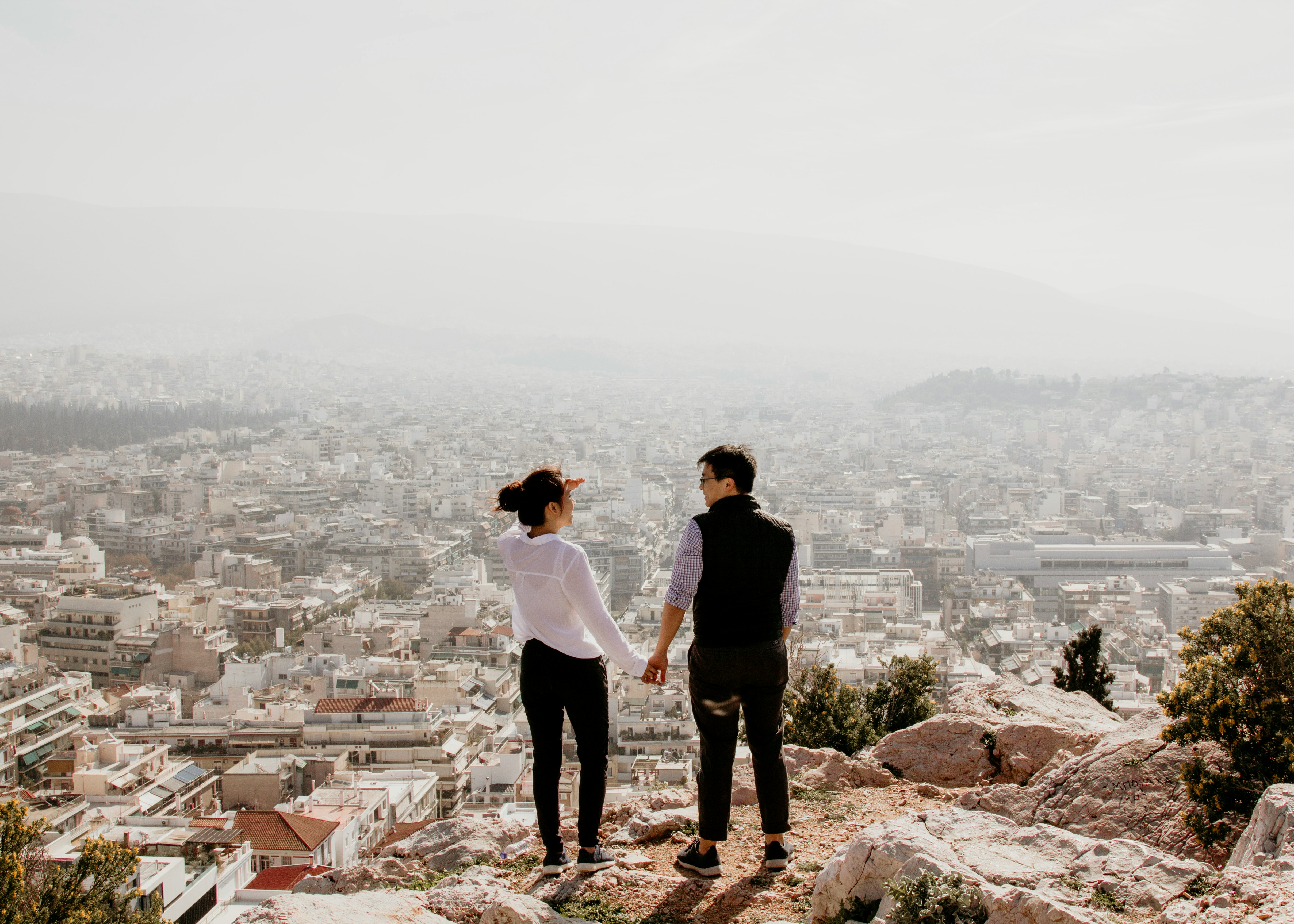 man and woman holding their hands together while standing on top of cliff