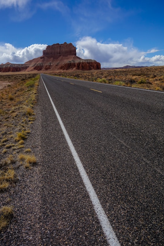 gray asphalt road near brown mountain under blue sky during daytime in Goblin Valley State Park United States