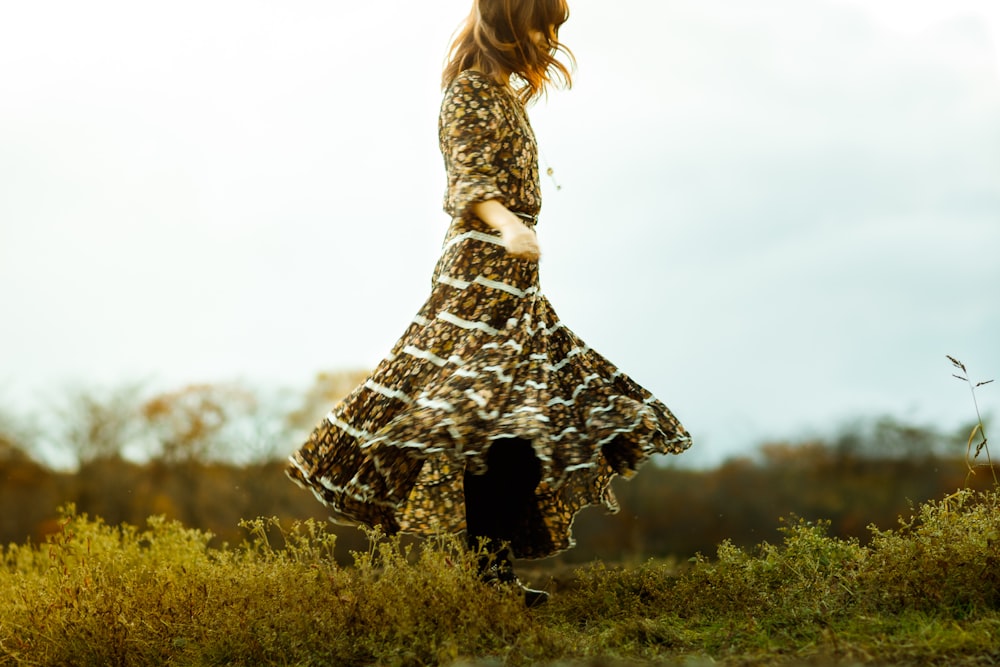 woman wearing brown and white long-sleeved long dress while standing on green grass