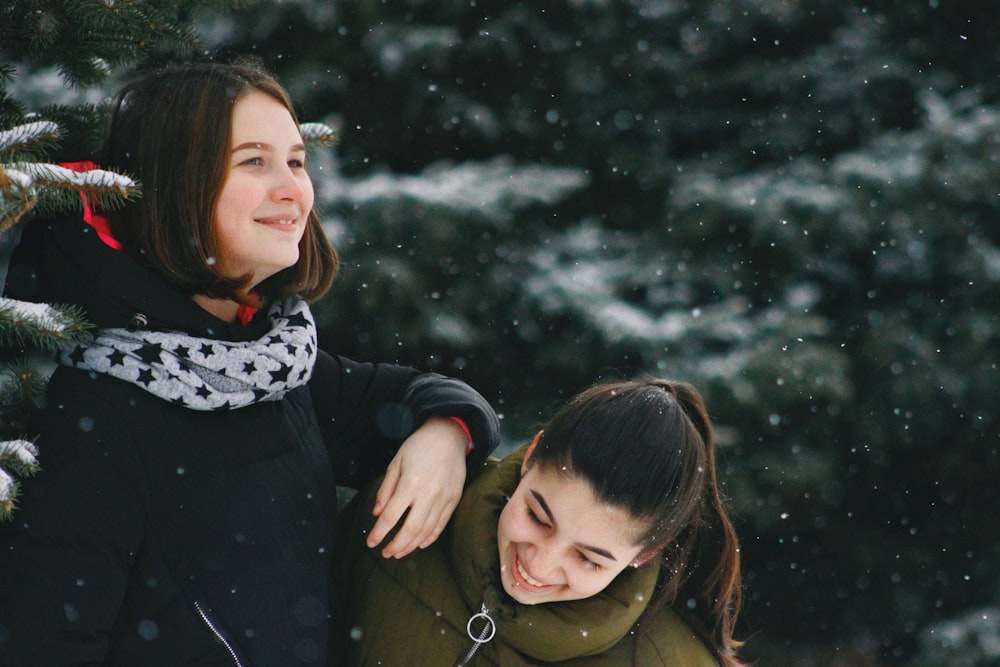 woman putting her arm to woman's shoulder beside tree