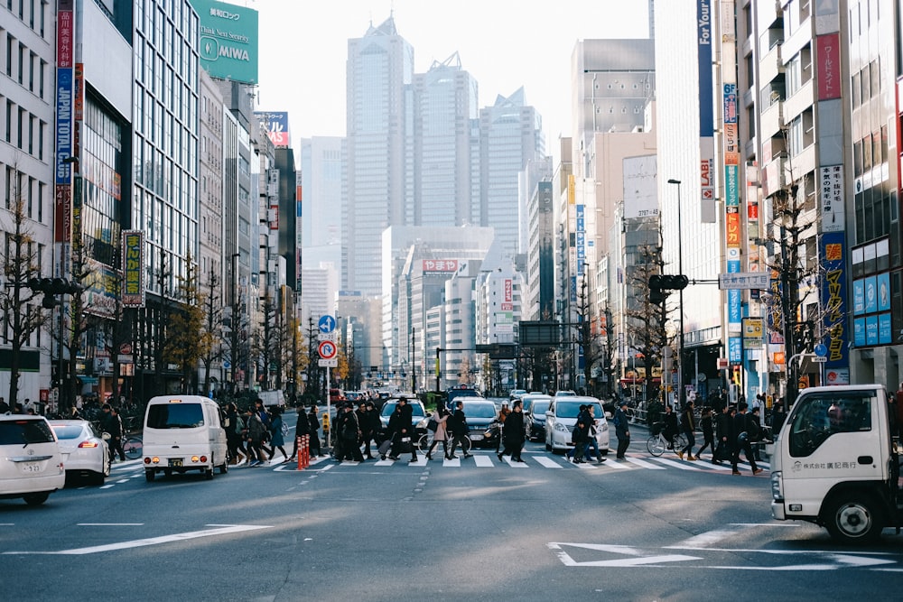 people crossing on road surround with buildings near parked car during daytime