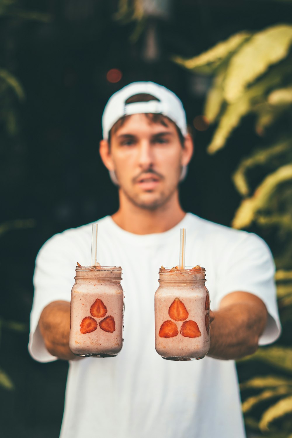selective focus photography of man holding two mason jars filled with beverage