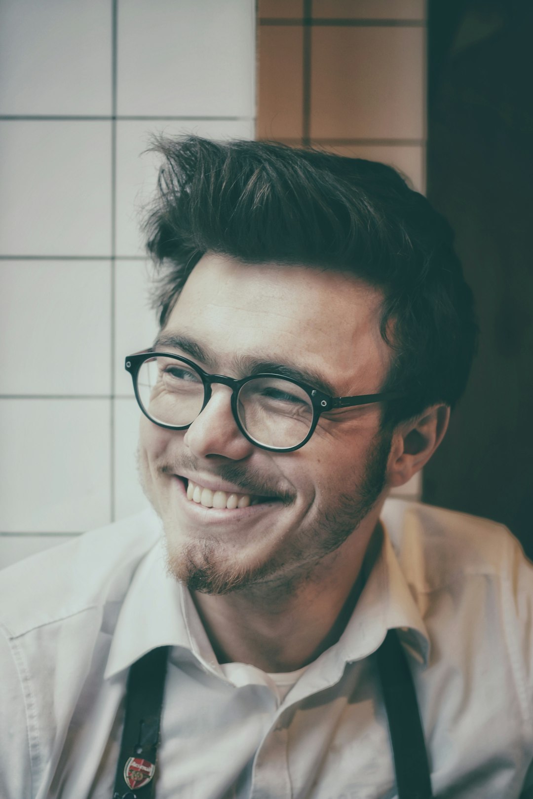 photo of man wearing black-framed eyeglasses beside wall tile