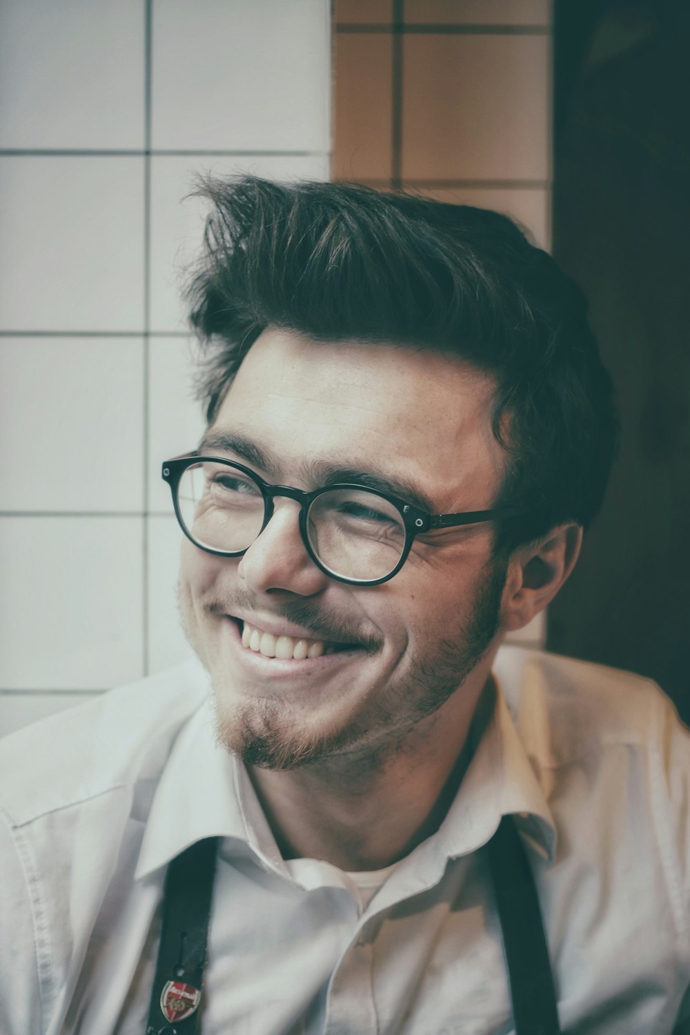 Foto eines Mannes mit schwarz gerahmter Brille neben einer Wandfliese