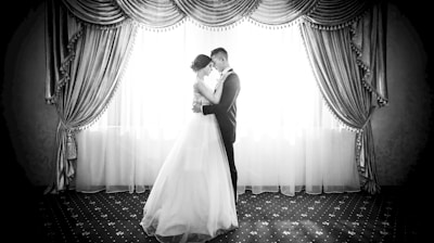 grayscale photography of couple facing in front curtain