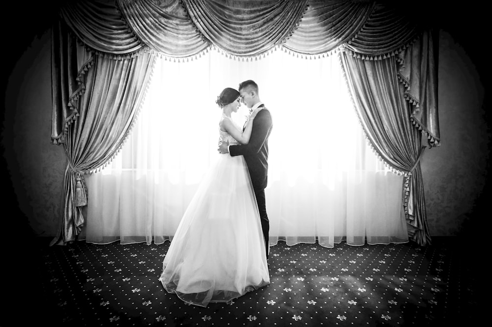 grayscale photography of couple facing in front curtain