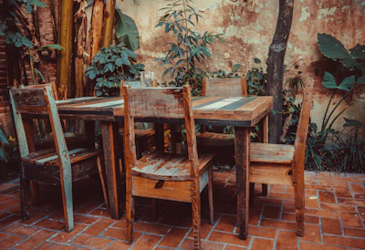 An outdoor patio set made of robust, weathered wood with green plants surrounding it.
