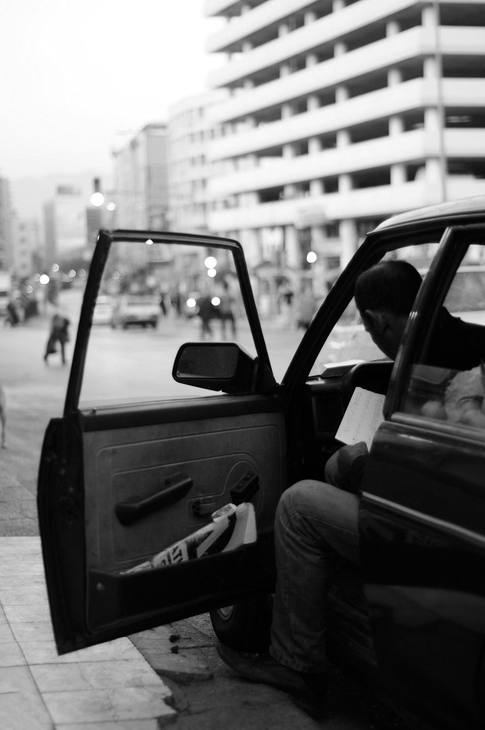 grayscale photography of man sitting inside car while door open