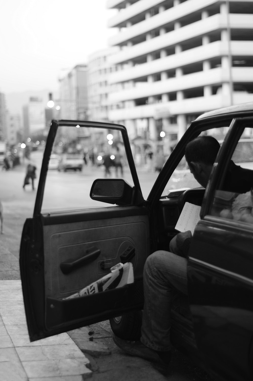 grayscale photography of man sitting inside car while door open