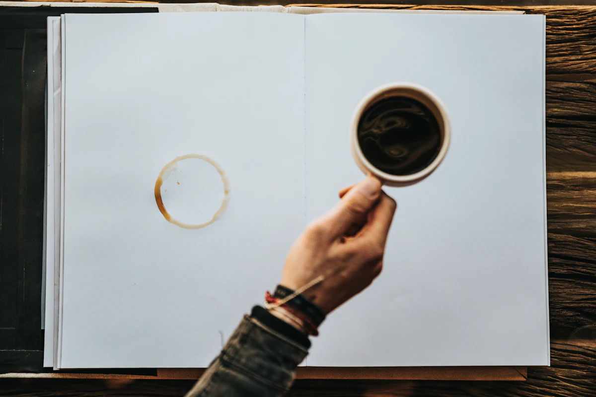 A person writing quietly at a desk with a notebook and coffee
