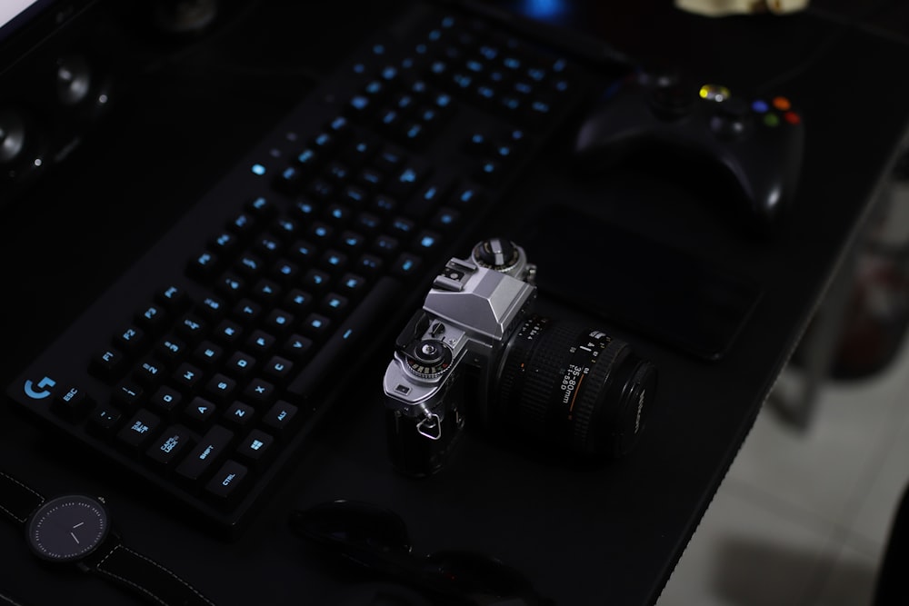 shallow focus photography of SLR camera, gamepad, and keyboard on top of table