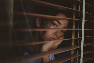 a woman looking out of a window with blinds