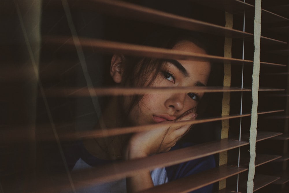 Une femme regardant par une fenêtre avec des stores