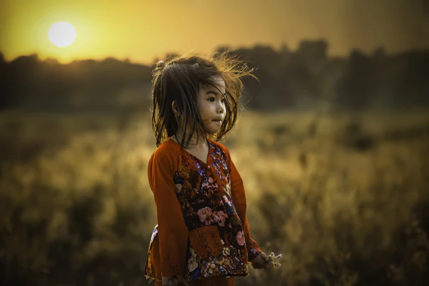 A soft golden light bathes a young girl standing confidently in a sunlit field, surrounded by gentle sparkles.