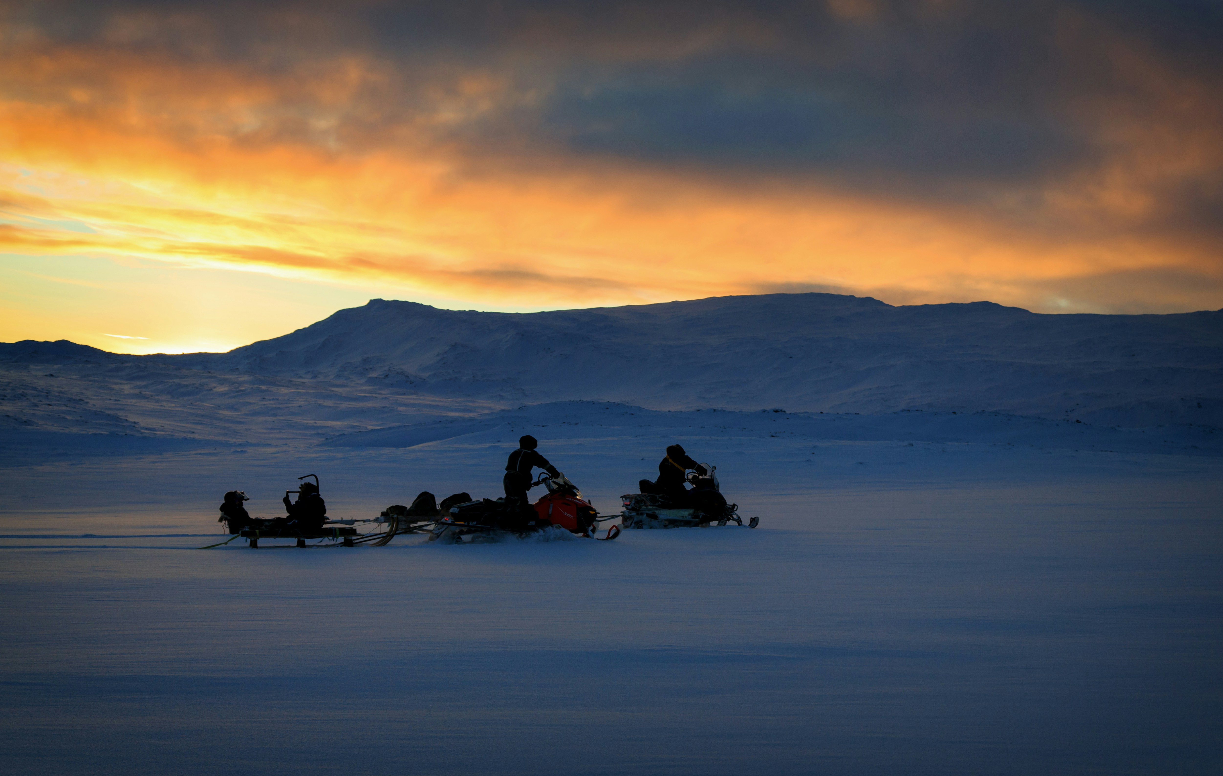 two men riding on snowmobile at sunset