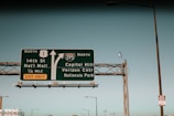 A highway sign directs drivers toward the National Mall and Capitol Hill, with arrows indicating separate routes. The sign is mounted on a metal framework, with a clear blue sky in the background. Additional street lamps and a smaller sign about snow emergency routes are visible.