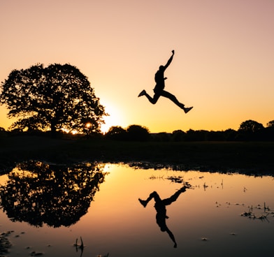 silhouette photo of man jumping on body of water during golden hour