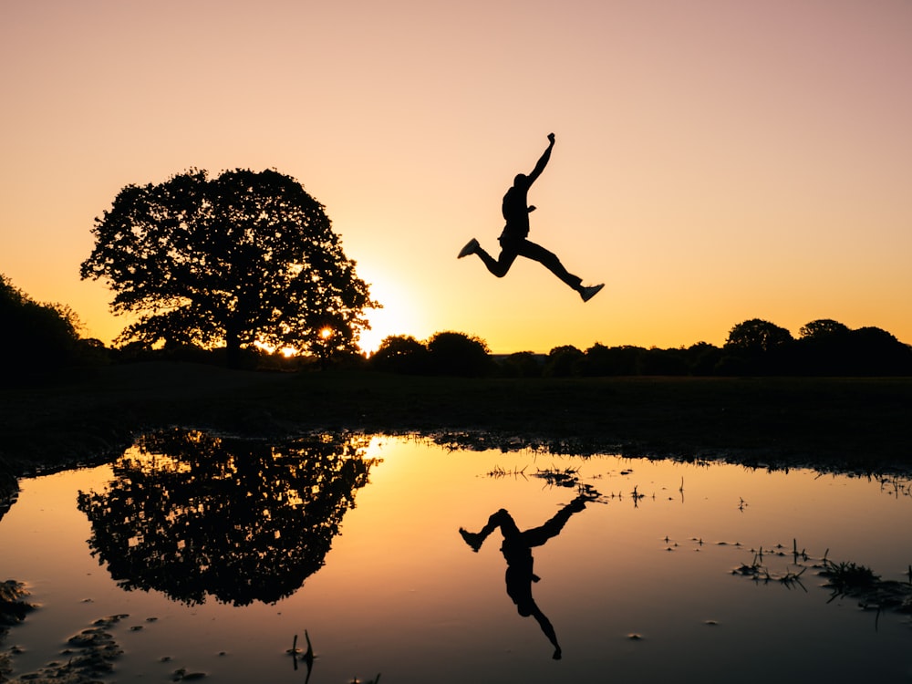Foto da silhueta do homem pulando no corpo da água durante a hora dourada
