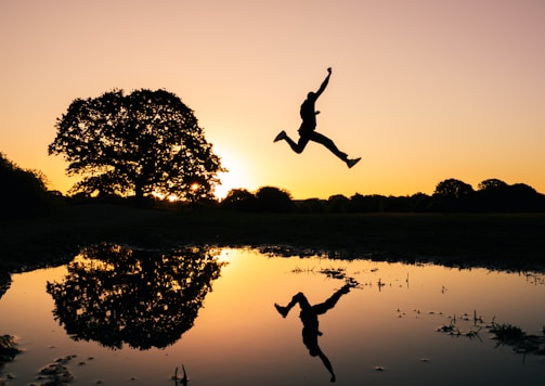 silhouette photo of man jumping on body of water during golden hour