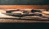 A collection of woodworking hand tools is spread on a wooden workbench. The tools include chisels, a hammer, a saw, and a plane, all lying amidst wood shavings. The background is slightly blurred, giving focus to the tools and wood shavings.